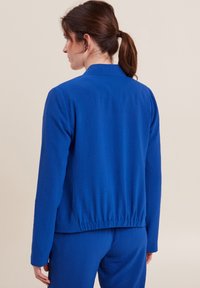 Felpa blu con maniche lunghe e orlo arricciato. Tessuto morbido, design del colletto semplice e dettagli minimi sul retro.