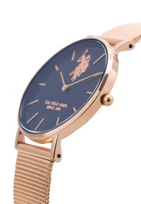 Orologio in oro rosa con quadrante blu navy, indicatori minimalisti e cinturino in maglia. Presenta un logo e una corona per le regolazioni.