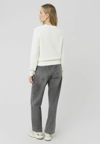 Pull blanc texturé avec un ourlet et des manches côtelés, associé à un jean gris taille haute et ample, et des baskets de couleur claire.
