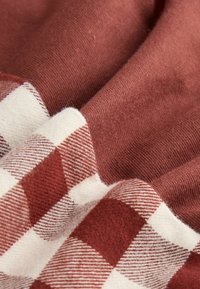 Teksturowana tkanina w ciepłym kolorze rdzy z kremowym wzorem w kratkę; miękka bawełniana tekstura, pomarszczona tkanina ukazująca wyraźne różnice w wzorze i odcieniach.