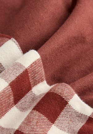 Teksturowana tkanina w ciepłym kolorze rdzy z kremowym wzorem w kratkę; miękka bawełniana tekstura, pomarszczona tkanina ukazująca wyraźne różnice w wzorze i odcieniach.