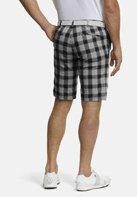 Schwarz-weiße karierte Shorts zeichnet sich durch ein gestreiftes Muster, Gesäßtaschen, einen Gürtelschlaufen und werden mit weißen Golfschuhen getragen.
