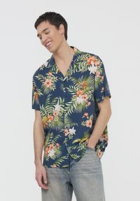 Camicia a manica corta blu navy con stampa floreale tropicale, caratterizzata da fiori rosa e bianchi, foglie verdi e una vestibilità rilassata.