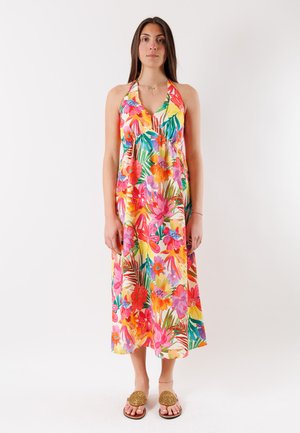 Mujer de pie vistiendo un vestido sin mangas, con cuello halter y largo medio, con un vibrante estampado floral multicolor y sandalias color tierra.