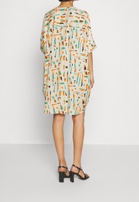 Robe à manches courtes, longueur genou en tissu beige clair avec des motifs géométriques multicolores en orange, vert et noir. Offre une coupe décontractée.