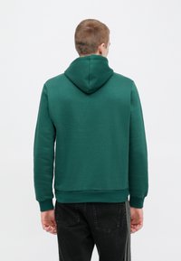 Πράσινο φούτερ με κουκούλα, κατασκευασμένο από απαλό ύφασμα. Διαθέτει άνετη εφαρμογή, ριμπ μανσέτες και μινιμαλιστικό σχέδιο χωρίς διακοσμητικά στοιχεία.