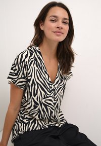 Zebra-patterned short-sleeve top in black and cream, featuring a deep V-neck and soft, textured fabric with a relaxed fit.