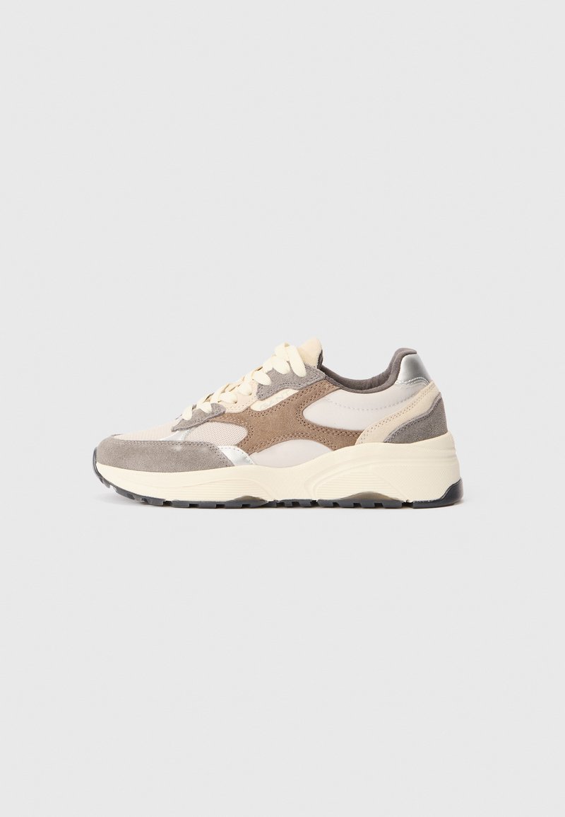 Baskets présentant un mélange de suède beige clair, marron et gris avec des accents métalliques, une semelle blanche épaisse et des lacets beiges plats.