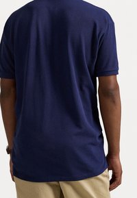 Námořnická modrá bavlněná tričko s texturovaným povrchem, krátkými rukávy a volným střihem, předváděné na osobě, která má na sobě béžové kalhoty.