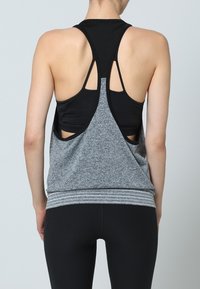 Svart och grå atletisk linne med racerback-design, utskärningar och randig fåll. Materialet verkar vara lätt och strukturerat.