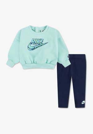 Lyseblå Nike sweatshirt med camouflage-logo kombineret med marineblå Nike leggings med logo nær anklen på en hvid baggrund.