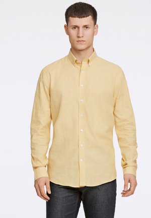 Camisa amarilla de botón, hecha de tejido texturizado, con cuello, mangas largas y dobladillo recto, combinada con jeans azul oscuro.