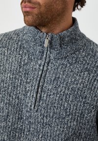 Sweter dzianinowy z wysokim kołnierzem i półzamkiem. Wykonany z teksturowanej włóczki w kolorze niebiesko-szarym z domieszką jaśniejszych i ciemniejszych włókien.