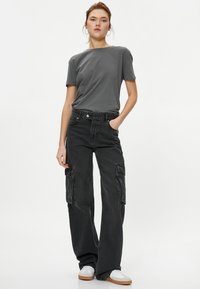 T-shirt gris, pantalon cargo noir ample avec poches latérales et baskets blanches. Texture de tissu lisse, design à jambes larges et accents simples.