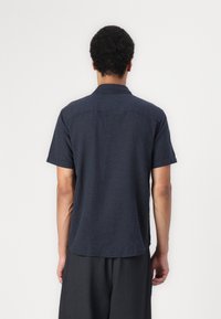 Chemise à manches courtes en tissu texturé bleu marine foncé, avec un col et un ourlet légèrement courbé. Design décontracté et léger.