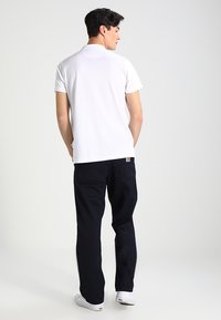 Witte polo met korte mouwen en navy broek met een relaxte pasvorm. Heeft een eenvoudig ontwerp en effen kleuren, aangevuld met witte schoenen.