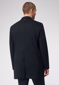 Blazer da uomo di un elegante blu navy scuro con una texture liscia, rever a scretto, con un'unica fessura e dettagli hardware minimi. Taglio pulito e su misura.