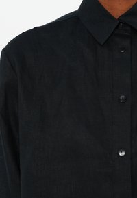 Black, button-up shirt featuring a classic collar, textured fabric, and black buttons along the front placket. Close-up view of details.