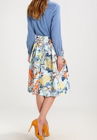 Blommig klänning med en ljusblå, plisserad kjol som har orange och gula blommor, tillsammans med en jeansskjorta och orange högklackade skor.