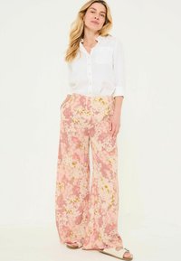 Flowy, floral-patterned pants in pastel pinks and yellows, paired with a white linen button-up shirt, displaying a relaxed fit and pockets.