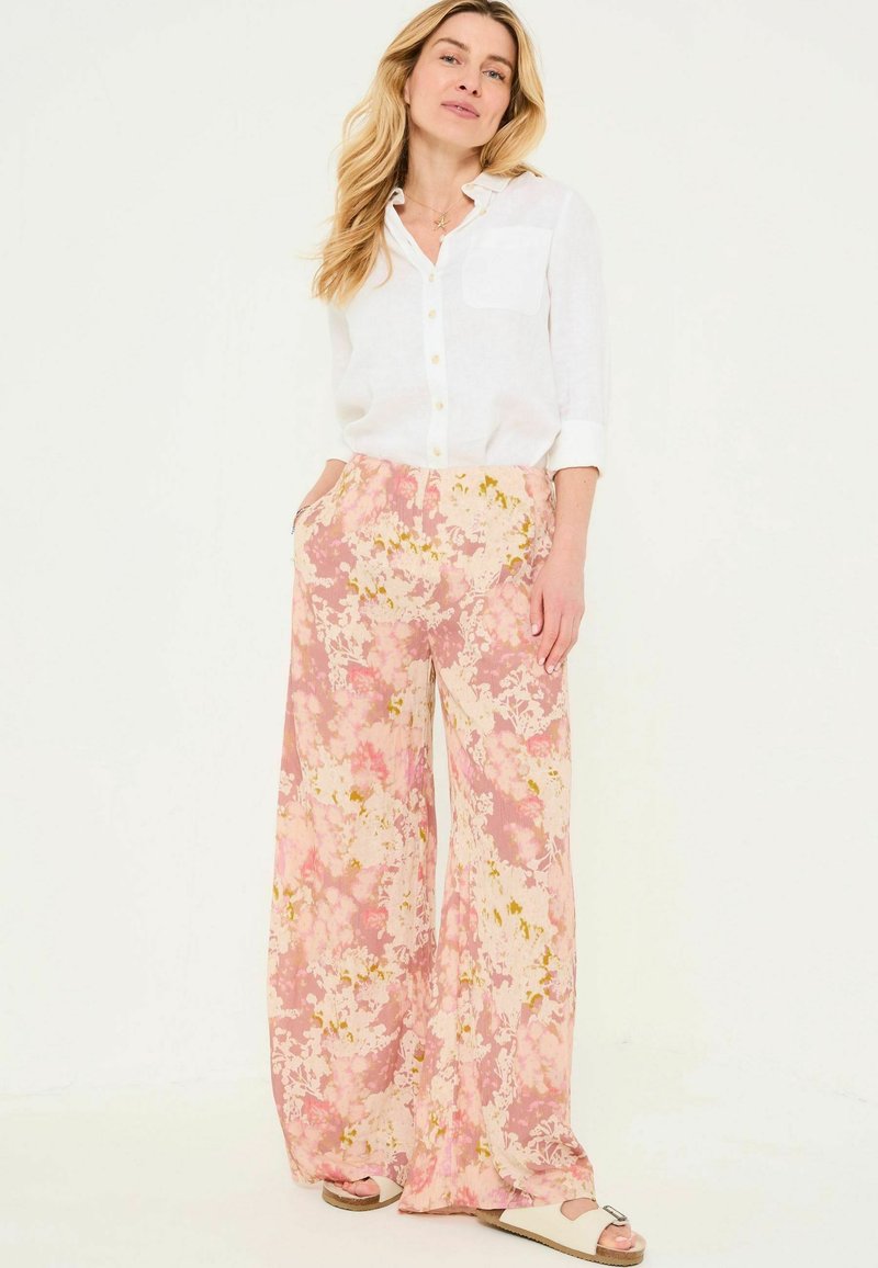 Flowy, floral-patterned pants in pastel pinks and yellows, paired with a white linen button-up shirt, displaying a relaxed fit and pockets.