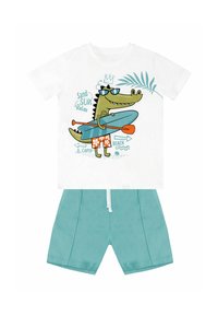 Hvid T-shirt med et cartoon krokodille i solbriller på en paddleboard, parret med lyseblå shorts. Behageligt stof, legende design.