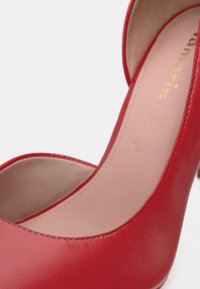 Κόκκινο δερμάτινο ψηλοτάκουνο παπούτσι με απαλή υφή, στρογγυλή μύτη και μπεζ πάτο. Το όνομα της μάρκας "Tamaris" χαραγμένο μέσα.