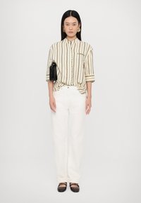 Striped beige button-up shirt with long sleeves, beige wide-leg jeans, and black flat shoes. Model holds a black bag. Simple jewelry accents.