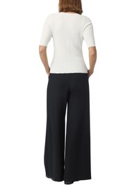 Witte ribbeltrui met korte mouwen gecombineerd met losse zwarte brede broek. Textuurstof en ontspannen silhouet.