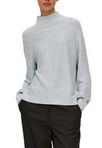 Helles graues, gestricktes Sweatshirt mit hohem Kragen und geripptem Saum; lässige Passform mit fallenden Schultern; glatte Textur; kombiniert mit dunklen Hosen.