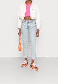 Bílá zkrácená džísková bunda se pruhovanými manžetami, růžový crop top, světle modré džíny s vysokým pasem, oranžová kabelka a vícebarevné tenisky.