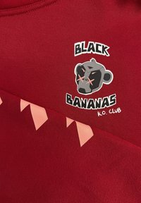 Rode sweatshirt met een grafisch ontwerp van een aap in een zwart en grijs kleurenpalet, en lichtroze driehoekige accenten langs de zoom.