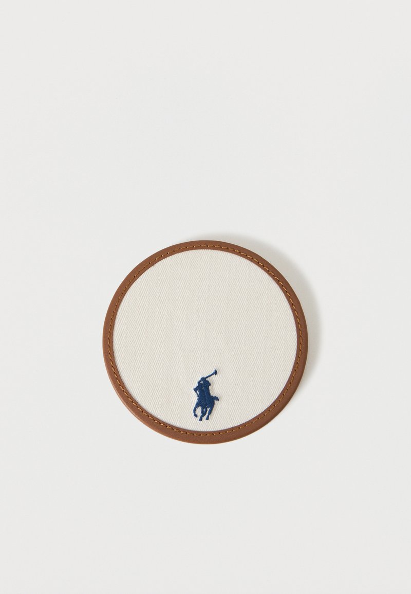 Στρογγυλή μπεζ υφασμάτινη επιφάνεια με καφέ δερμάτινη περίμετρο, που διαθέτει μικρό σήμα με κέντημα μπλε σκούρου παίκτη πόλο στο κάτω κέντρο.