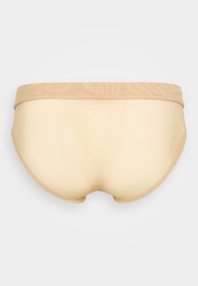 Bēša bezšuvju apakšbikses ar gludu tekstūru un platām elastīgām jostām, ar minimālām šuvēm un zemu vidukļa griezumu komfortam.