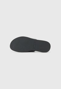 Black rubber sole with a textured surface and slightly curved shape. Features a rectangular brand label near the heel.