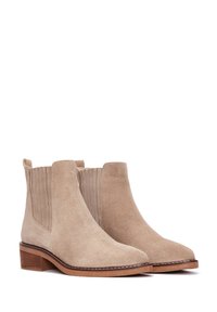 Bottines en suède beige avec des panneaux latéraux élastiques, un talon en bois empilé et des coutures contrastantes le long de la semelle. Texture lisse.