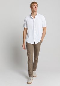 Witte korte mouwen button-up shirt, gecombineerd met tan slim-fit broek en lichtgekleurde sneakers, die een relaxte pasvorm en soepele textuur tonen.