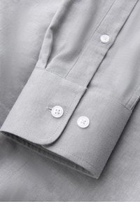 Poignet de chemise gris clair avec deux boutons blancs, coutures soignées et un motif géométrique hexagonal discret sur le tissu.