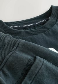 Tume roheline sviiter ribitud kaeluse ja varrukatega. Omab tikkimislogot kaeluse ääres ja tekstuuriga kangajooni.