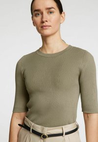 Khaki rebrasti pleten top z okroglim izrezom in kratkimi rokavi. Usklajen z visokimi bež hlačami in črnim pasom.