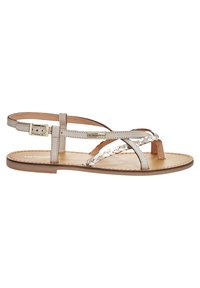 Sandal in pelle beige con design a strappo intrecciato, con punta a post e fibbia regolabile alla caviglia. Texture liscia con suola piatta.