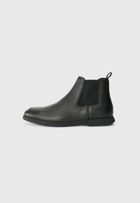 Bottines en cuir noir avec une texture lisse, des panneaux élastiques sur les côtés et une languette à l'arrière. Bout arrondi et semelle en caoutchouc.