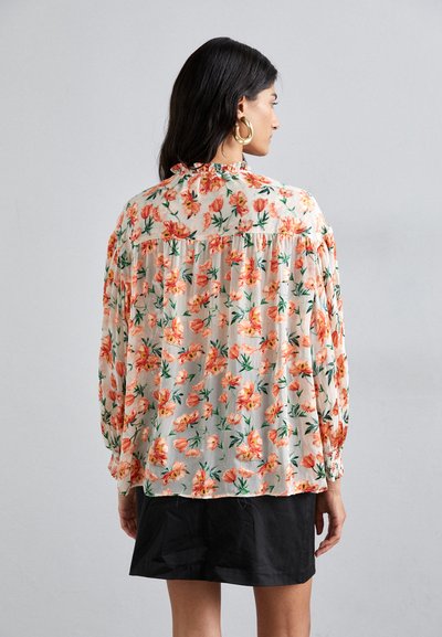 Blusa floral en un tejido ligero y semitransparente, con un patrón de flores en tonos durazno y verde, mangas largas y un diseño fruncido en la parte trasera.