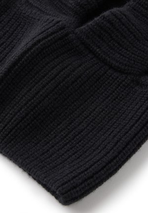 Close-up af sort ribstrikket stof med foldet kant, der viser bløde, teksturerede uldfibre og syningsdetaljer.