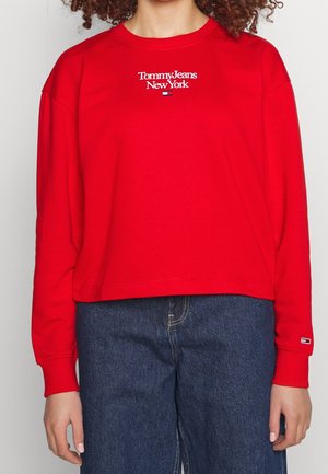 Rød cropped sweatshirt med lange ærmer med "Tommy Jeans New York" tekst og logo, kombineret med højttaljede blå jeans.
