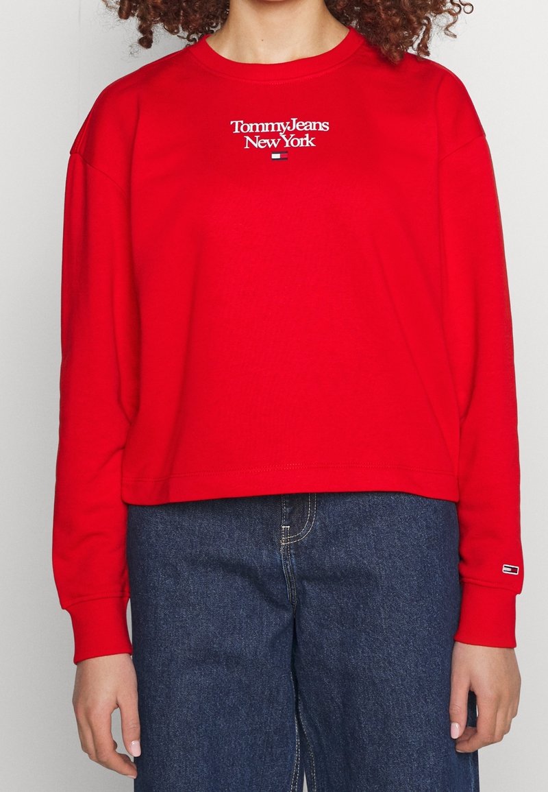 Sweat-shirt court rouge à manches longues avec le texte et le logo "Tommy Jeans New York", associé à un jean bleu taille haute.