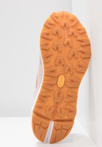 Semelle en caoutchouc orange d'une chaussure avec des motifs de bande de roulement multidirectionnels et le logo Vibram au centre, positionnée verticalement sur un fond blanc.