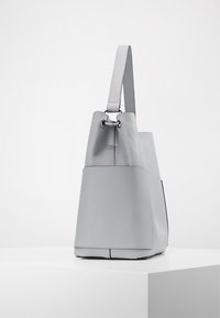 Sac fourre-tout en cuir gris avec une forme structurée, doté d'une poignée supérieure, de garnitures métalliques et d'une poche extérieure pour l'organisation.