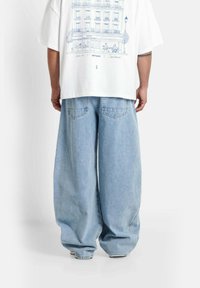 Luźne, jasnoniebieskie dżinsy o teksturze dżinsu, z dwoma tylnymi kieszeniami i elastycznym paskiem w talii, zestawione z białym T-shirtem z graficznym nadrukiem.