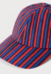 Κόκκινο, μπλε και μαύρο ριγέ καπέλο με στρογγυλεμένο κορυφαίο μέρος, λεπτομέρειες με ραφές και καμπυλωτό γείσο. Το ύφασμα δείχνει υφή και είναι ελαφρύ.